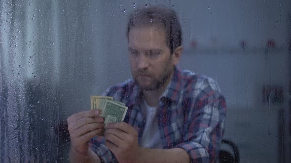 Middle-Aged Man Counting Money Behind Rainy Window, Poor Budget, Poverty