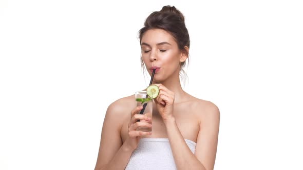 Healthy Caucasian Girl Drinking Water with Cucumber From Glass Over White Background in Slowmotion