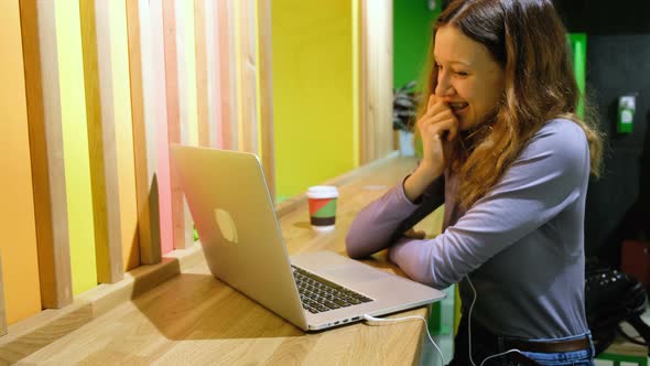 Girl Is Talking on Skype or Video Connection with a Loved One, Smiling and Waving To the Laptop