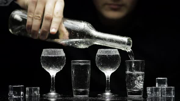 Barman Pour Frozen Vodka From Bottle Into Glasses with Ice. Black Background