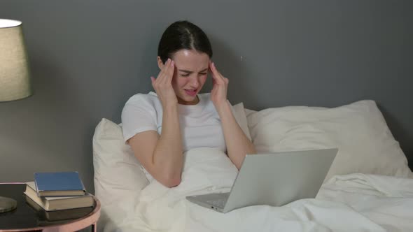 Young Woman with Laptop Having Headache in Bed 