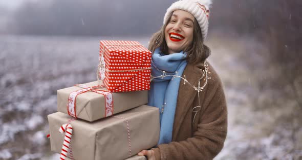 Portrait of a Happy Woman with Gift Boxes on the Snowy Field