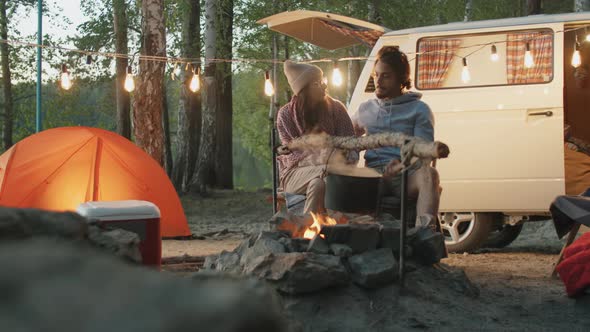 Couple Talking at Campsite while Cooking Food over Fire