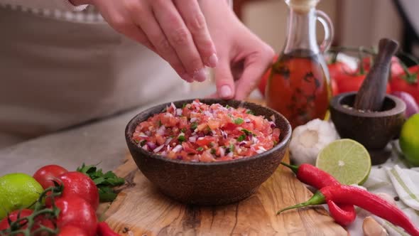 Woman Salting Salsa Dip Sauce in Wooden Bowl at Domestic Kitchen