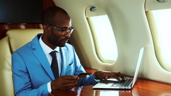 Businessman making online payment on airplane with credit card