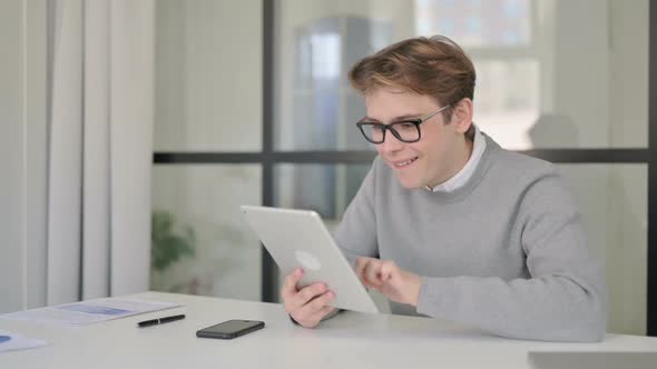 Young Man Celebrating Success on Tablet in Modern Office