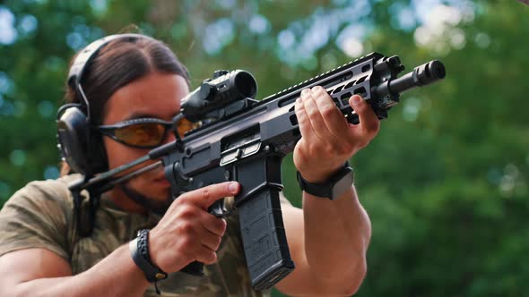 White Muscular Man in Camouflage Tshirt and Safety Gear Firing Submachine Gun on Training Ground