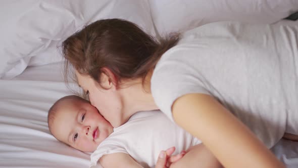 Loving Young Mommy Hugging Soothing Adorable Sweet Baby Girl Lying in Bed