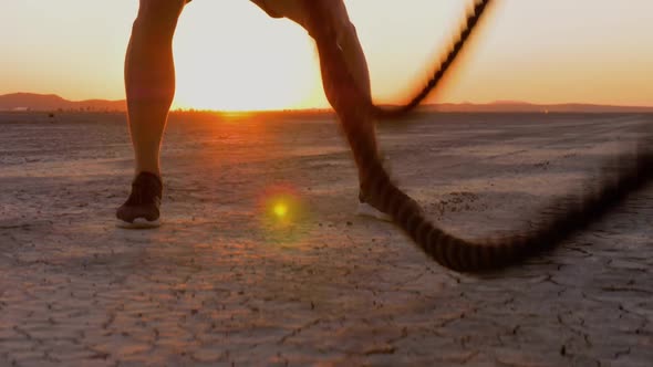 Athletic man working out with battle ropes on a dry lake at sunset