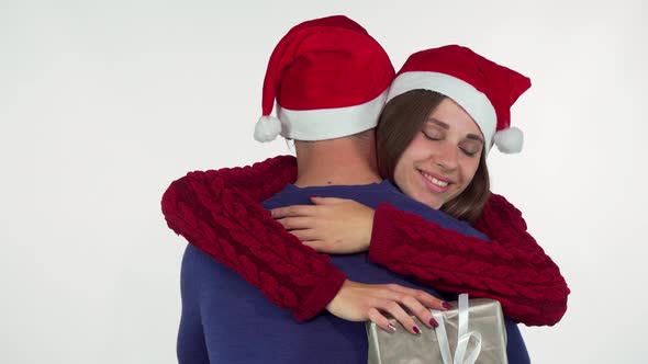 Charming Young Woman in Christmas Hat, Holding Her Present Hugging Her Man