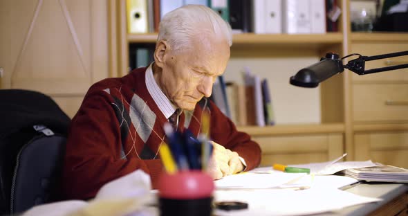 Senior Businessman Writing on Paper at Table in Office