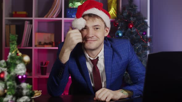 Young Man in Santa Hat Plays with Pompom Sitting in Office