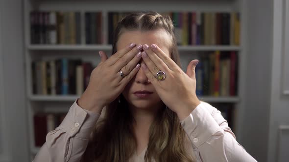 Portrait of Serious Caucasian Lady Who Closes Eyes By Hands and Open Them Sitting in Room