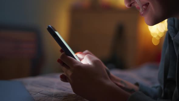 Close-up view of smiling woman texting by phone on the bed