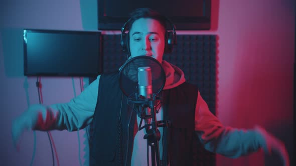 A Man in Hoodie Rapping in the Record Studio Gesticulates While Recording His Track