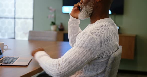 Senior man talking on mobile phone while using laptop 4k