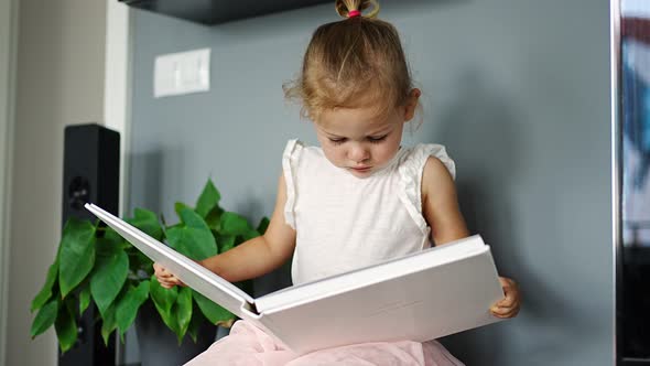 Happy Cute Little Girl Looking at Photos in Album alt