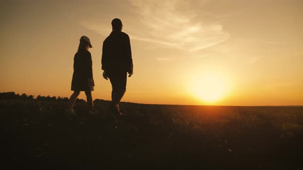 Young Mother Farmer Teaches Her Daughter To Work in a Wheat Field. Silhouette of a Farmers Family in