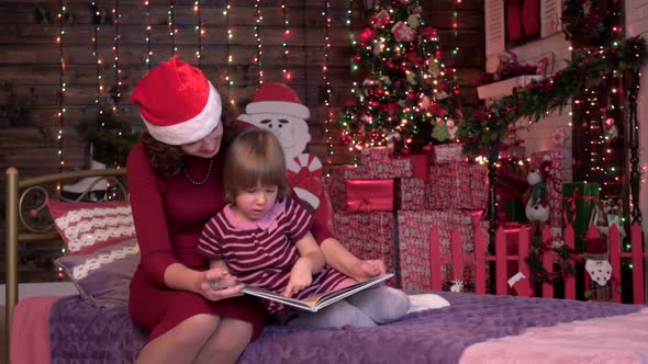 Caring Mother Reading a Book with Her Girl in the Bedroom, New Year Decorations, Lights