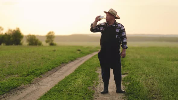 Senior Worker in Apron Holding Drinking Beer at Field