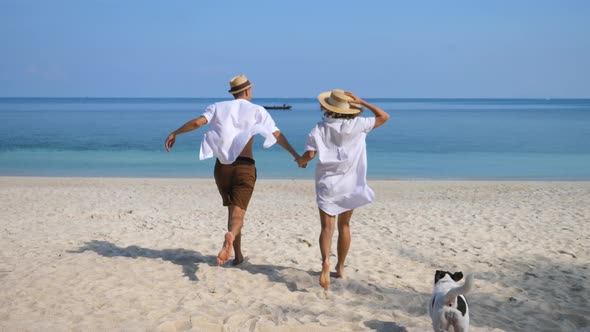 Happy Couple Running On The Beach With Dog On Vacation In Honeymoon