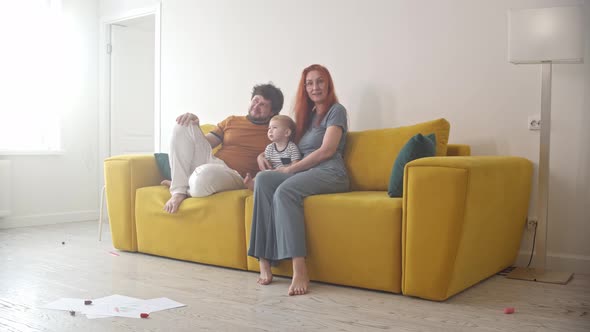 Family with a Little Baby Sitting on Yellow Couch and Watching TV