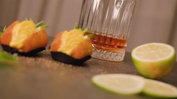 Cakes in Paper Cups Lie on Table Near Lime and Drink Glass