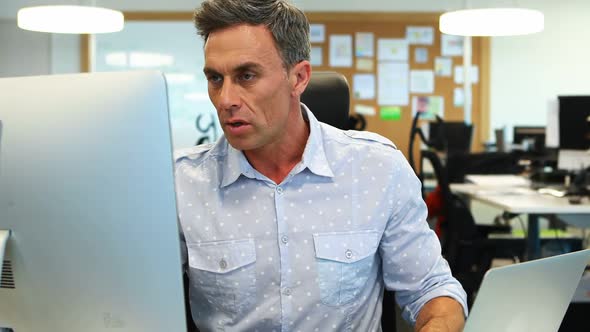 Male executive working on laptop and computer at desk