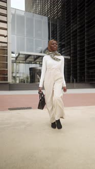 Black Woman in Smart Casual Wear and Hijab Walking Near Skyscraper