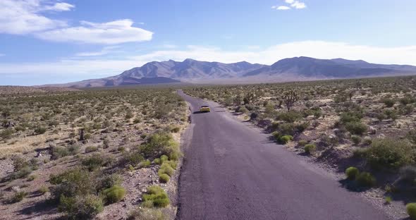 Aerial view of yellow sport car driving on asphalt road in the middle of dusty dry desert land.