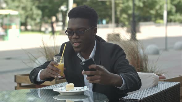 Smiling Young Businessman Sitting at Coffee Shop Using Mobile Phone, Taking Selfie