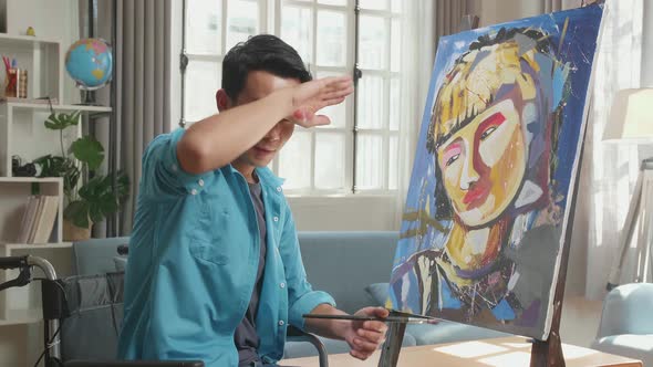 Artist Man In Wheelchair Turn To Wipe The Sweat And Smiling While Painting A Girl On The Canvas