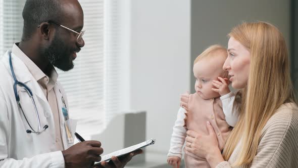 Woman with Baby Having Consultation with Male Doctor in Clinic