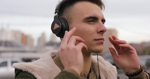 Young Man Listening the Music Puts on Headphones in City