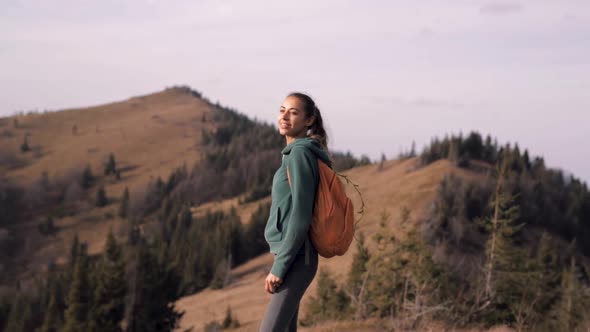 Woman Hiker Standing on Edge of Mountain Ridge Against Background of Sunset