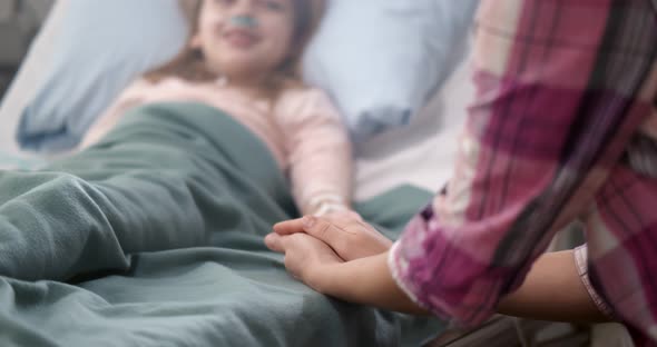 Mother Holding Child's Hand Lying in Bed in Hospital To Give Encouragement