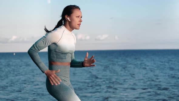 Athletic Woman Jogger Running at Nature Beach Sea Landscape Listening Music in Headphones