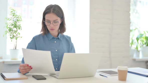 Young Woman Working on Laptop and Reading Documents in Office