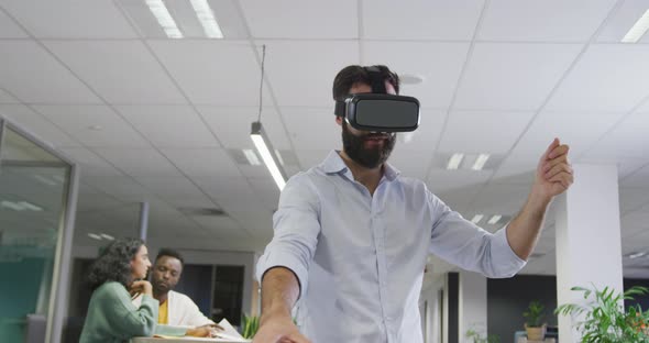 Happy biracial businessman using vr headset over colleagues in office