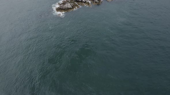 An aerial revealing capture of The Muglins Lighthouse during a cloudy day.