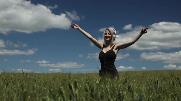 Blonde woman in headphones dancing in wheat field in summer time