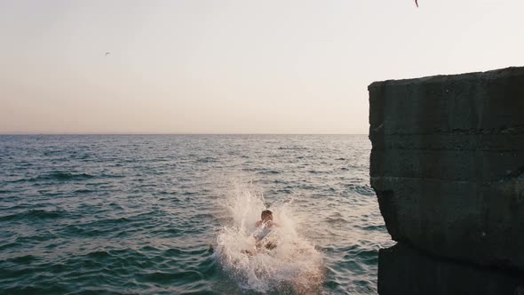 Young Woman and Man Synchronously Doing Backflip From a Pier Into the Sea During Beautiful Sunrise