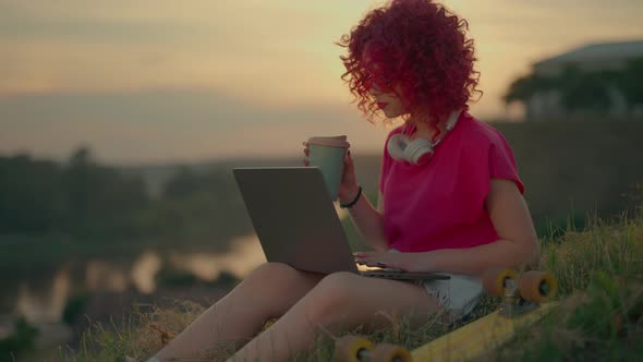 A Pink Curly Girl is Working or Studying on Laptop Outdoors