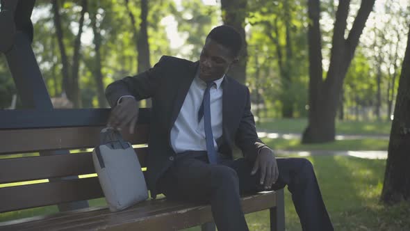 Tired African American Man in Business Suit Putting Bag on Bench and Looking Away. Portrait of