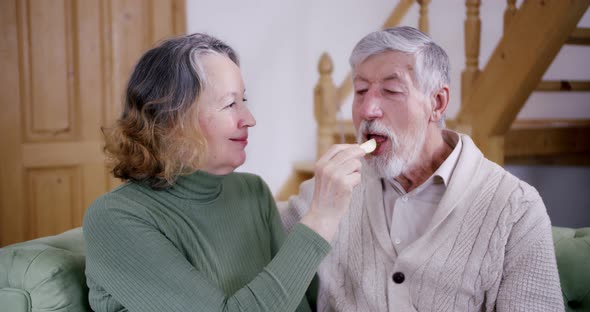 Portrait of an Elderly Couple Wife with Her Hands Feeds Her Old Husband with Gray Hair and Smiles He