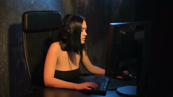 Serious Woman Gamer Playing Online Game on a Pc Computer Wearing Headset and Talking with a Team