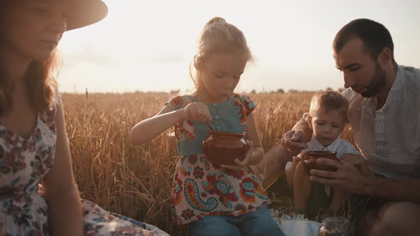 A Young Happy Family with Children is Relaxing on a Picnic in a Wheat Field and Eating the Food They