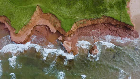 Topdown aerial view descending on the ocean coastline as waves of water crash into the shore and roc