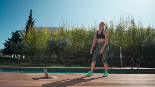 Young Caucasian Woman in the Park Practicing Jumping with Personal Trainer Online Via Laptop