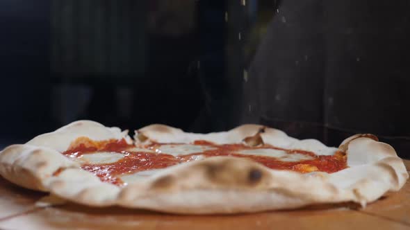 Close-up of Chef Pouring Seasonings on Baked Cooked Readymade Pizza at Italian Restaurant Kitchen in